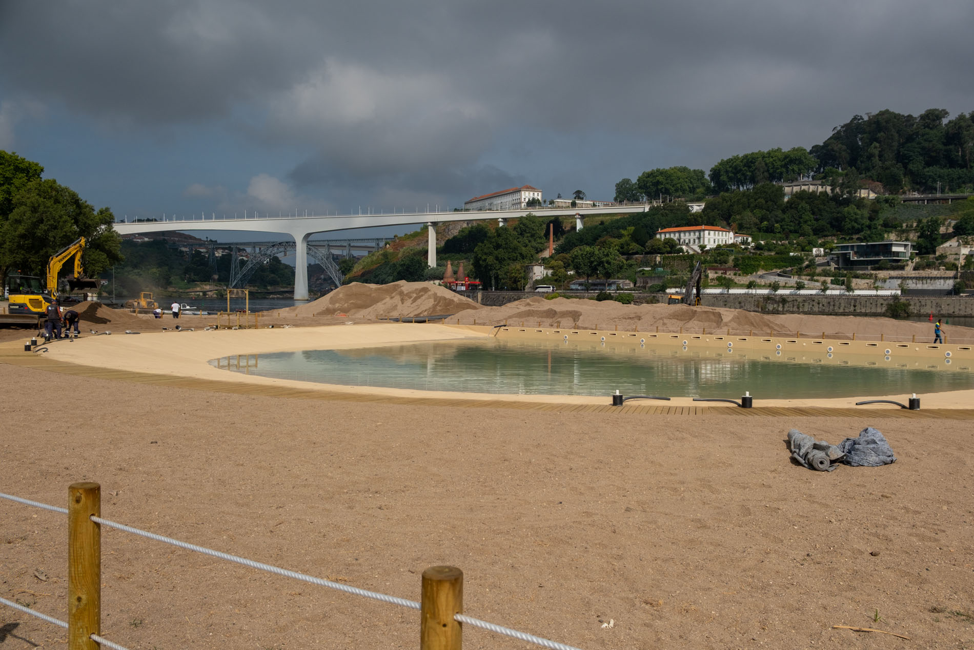 Piscina do Areinho one day before opening, with workers, machinery and the Douro riverfront beyond.
