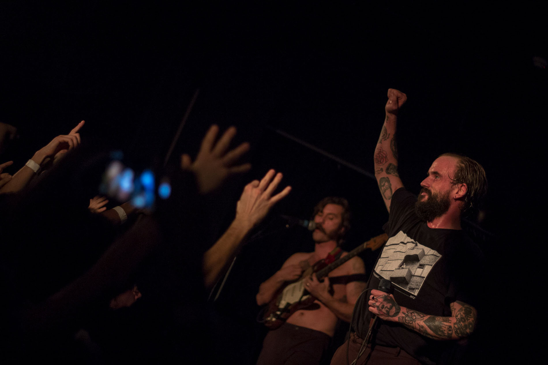 IDLES vocalist raising his fist as audience members reach toward the stage.