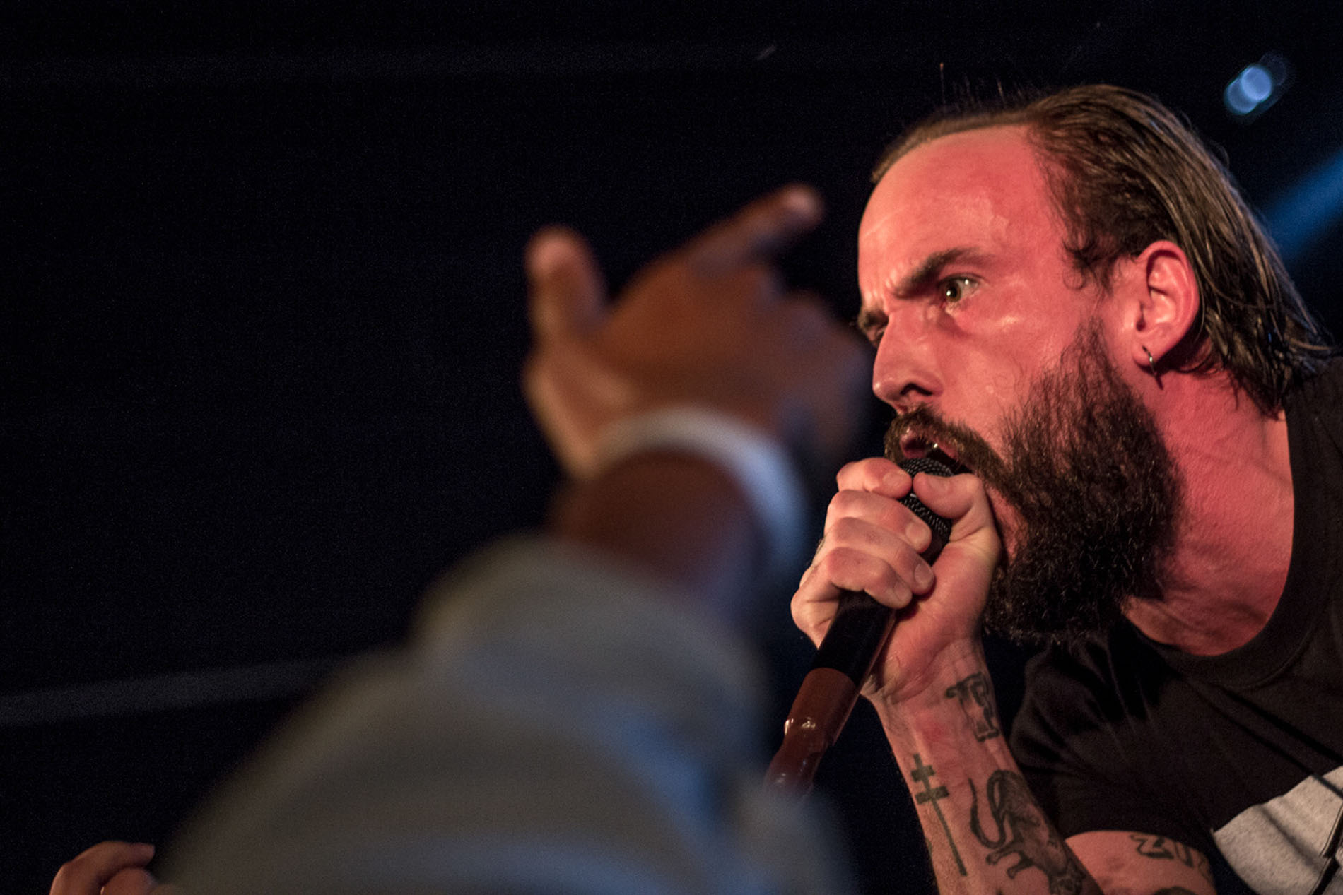IDLES vocalist singing close to the audience with a raised hand in the foreground.